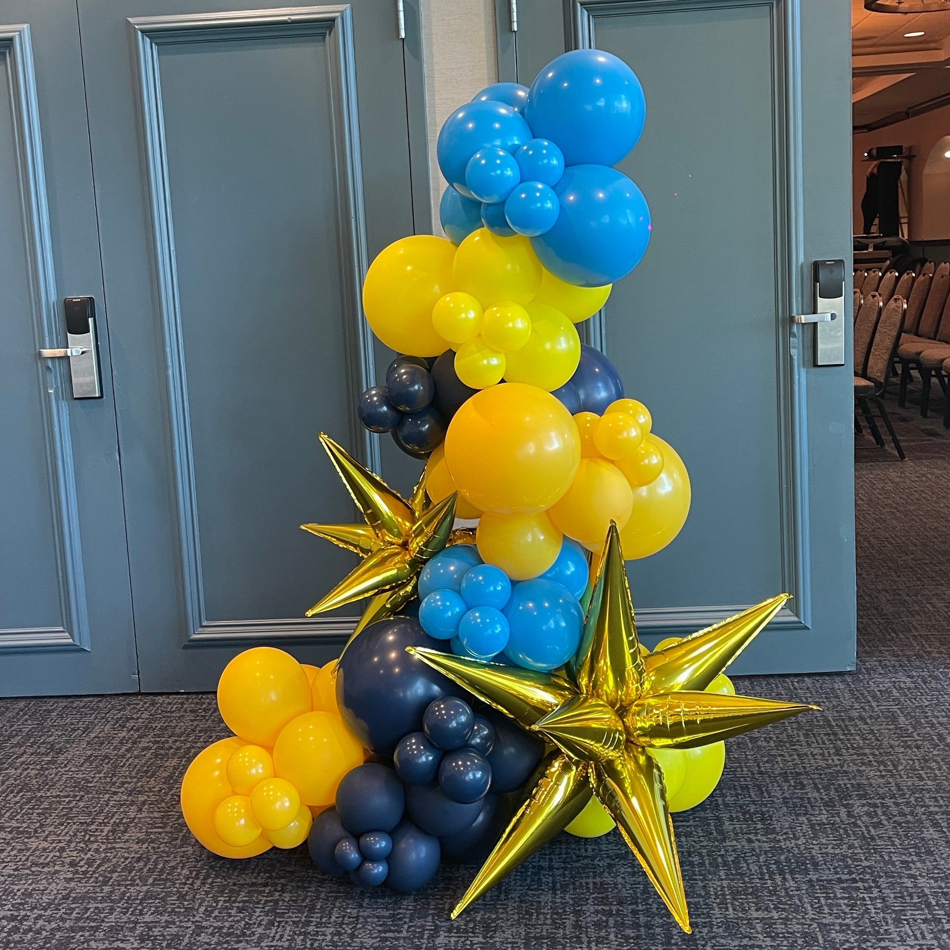 Custom free-standing balloon garland in blue, navy, and yellow with gold foil exploding stars
