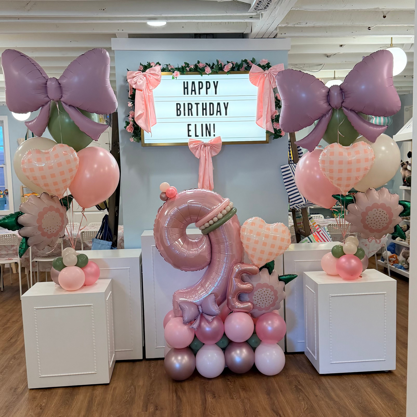 Pink balloon marquee stacker and helium bouquets with 'Happy Birthday Elin!' sign in a store setting
